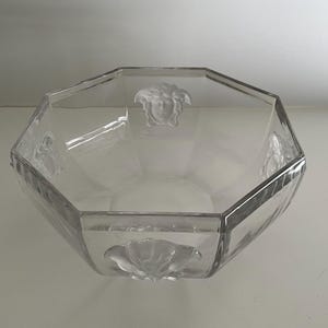 Puede incluir: Cuenco de vidrio transparente, octogonal, con dise&ntilde;os en relieve de cabeza de Medusa y flores. El cuenco tiene un dise&ntilde;o facetado y probablemente se utiliza con fines decorativos o para servir.
