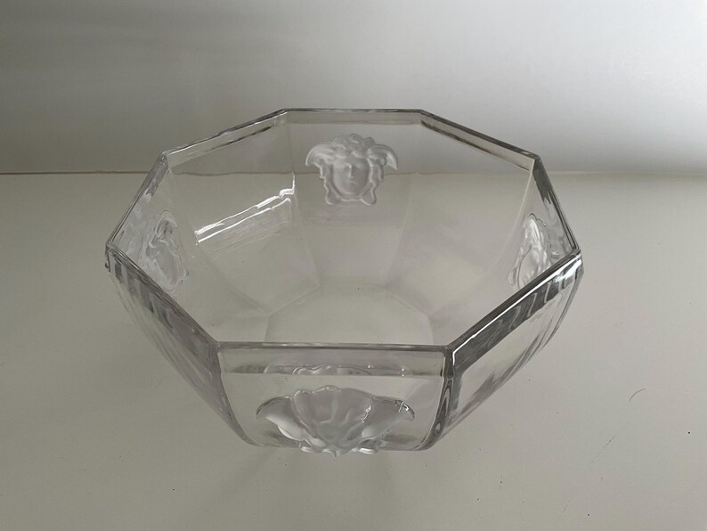 Puede incluir: Cuenco de vidrio transparente, octogonal, con dise&ntilde;os en relieve de cabeza de Medusa y flores. El cuenco tiene un dise&ntilde;o facetado y probablemente se utiliza con fines decorativos o para servir.