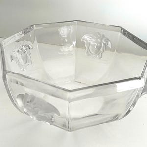 Puede incluir: Cuenco de vidrio transparente, octogonal, con detalles en relieve de cabezas de Medusa. El cuenco tiene un dise&ntilde;o geom&eacute;trico y probablemente se utiliza para servir o exhibir. El vidrio transparente permite la visibilidad del contenido.