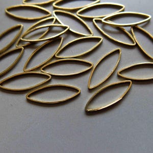 Pode incluir: Um grupo de contas ovais de metal dourado, espalhadas sobre uma superfície branca.