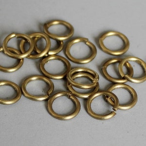 May include: A group of 14 gold-colored metal jump rings. The rings are all the same size and are arranged in a random pattern.