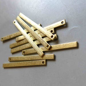 May include: A group of ten gold-colored metal bars with rounded ends and small holes. The bars are stacked on top of each other, creating a pile.