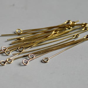 Può includere: Un mucchio di spilli per la testa dorati con un anello a un'estremità. Gli spilli sono lunghi circa 2,5 cm.