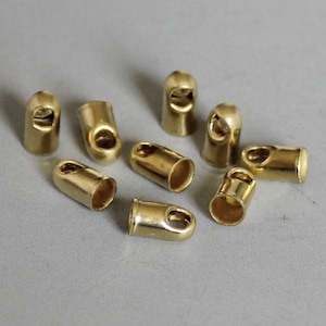 May include: A group of ten gold-colored metal end caps for cords or ropes. The end caps have a small hole in the center.