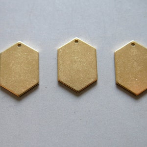 Puede incluir: Tres etiquetas hexagonales de metal de color dorado con un agujero en la parte superior para colgar.