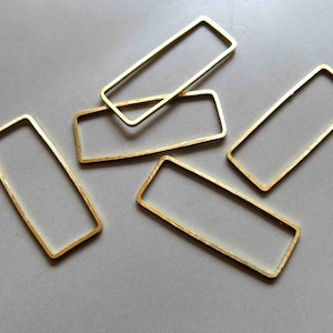 Puede incluir: Cinco marcos rectangulares de metal de color dorado de diferentes tamaños. Los marcos están dispuestos en un patrón aleatorio sobre una superficie gris.