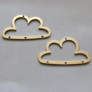 Könnte beinhalten: Zwei goldfarbene Metall-Anhänger in Wolkenform mit jeweils drei Löchern.