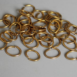 May include: A pile of gold-coloured metal jump rings. The rings are oval-shaped and have a smooth finish.
