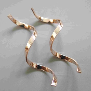 May include: A pair of long, gold-toned earrings with a twisted, wavy design.