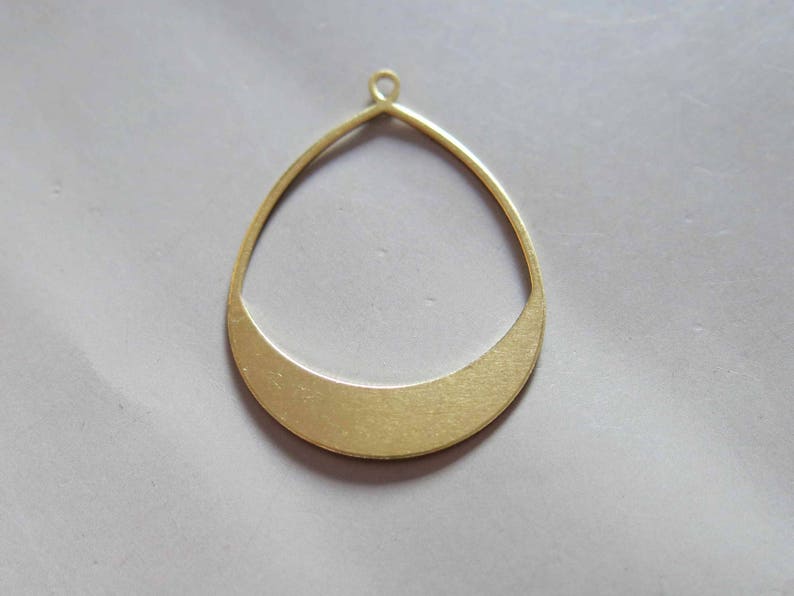 May include: A gold-colored metal pendant shaped like a teardrop with a rounded bottom. The pendant has a smooth, polished finish.