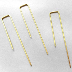 Può includere: Tre forcine per capelli color oro a forma di U, disposte su una superficie grigio chiaro. Le forcine sono sottili e hanno un design semplice e minimalista. Le forcine sono in metallo e hanno una finitura lucida.
