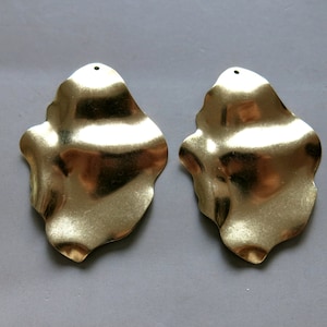 May include: A pair of gold-toned earrings with a wavy, organic shape. The earrings are made of metal and have a shiny finish.