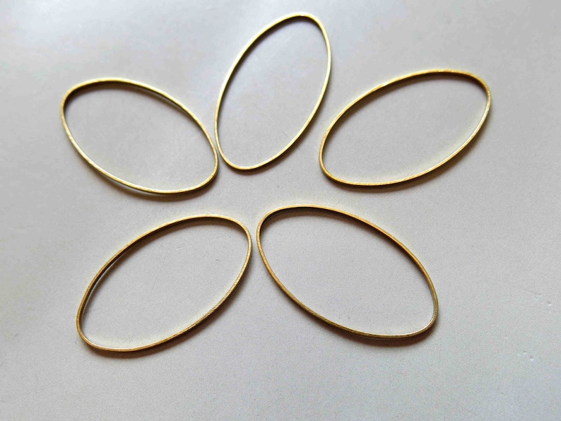 Pu&ograve; includere: Cinque anelli di metallo ovali dorati, disposti a forma di stella su uno sfondo bianco.