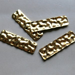 May include: Four gold-colored metal rectangular shapes with a textured surface. The shapes are scattered on a white background.