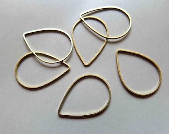 Könnte beinhalten: Sechs goldfarbene Metallringe in Tropfenform. Die Ringe sind alle unterschiedlich groß und liegen in einem zufälligen Muster auf einer weißen Oberfläche.