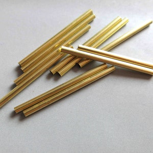 以下が含まれることがあります： さまざまな長さの10本の金色をした金属製のチューブのグループ。チューブは薄い灰色の表面にランダムに配置されています。