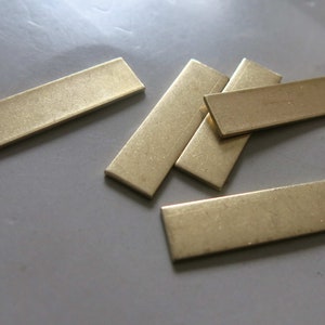 May include: Five rectangular brass bars, all the same size and shape, are stacked on top of each other. The bars are a light gold colour and have a slightly textured surface.