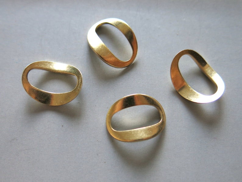 May include: Four gold-colored metal rings with a rounded oval shape and a hole in the center. The rings are arranged in a semi-circle on a gray surface.