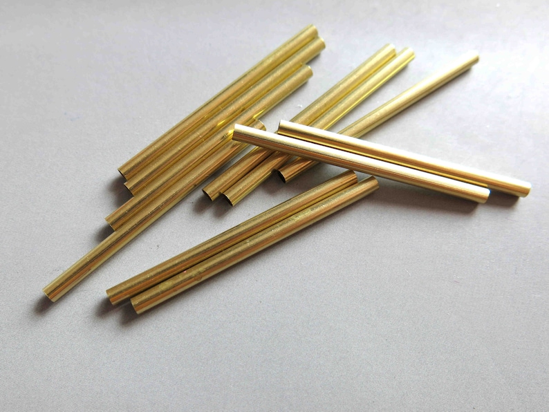 May include: A group of ten gold-coloured metal tubes of varying lengths. The tubes are arranged in a random pattern on a light grey surface.