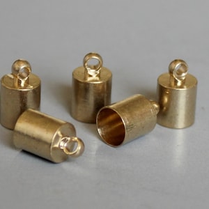 Puede incluir: Cinco tapones de extremo de metal de color dorado con un bucle en la parte superior. Los tapones de extremo son cilíndricos y tienen un acabado liso.