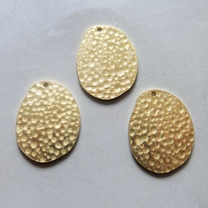Puede incluir: Tres abalorios de metal ovalados de color dorado con textura martillada.