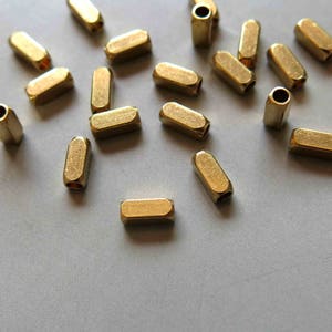 Op de afbeelding: Een verzameling gouden metalen afstandhouders, elk met een cilindrische vorm en een licht afgeronde rand. De afstandhouders zijn gerangschikt op een lichtgrijze ondergrond.