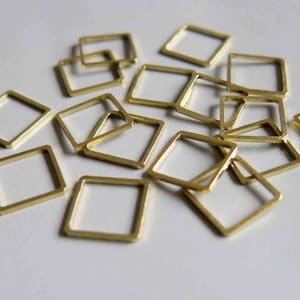 Puede incluir: Un grupo de anillos de salto de metal dorado, también conocidos como anillos partidos, están dispersos sobre una superficie blanca. Los anillos son todos del mismo tamaño y forma, y están dispuestos en un patrón aleatorio.