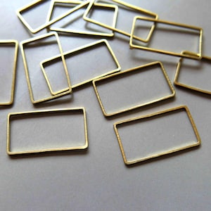 May include: A collection of gold-toned metal rectangular frames of various sizes. The frames are arranged in a random pattern on a white surface.