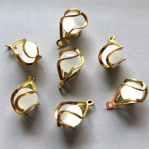 Puede incluir: Siete tapas de cuentas de metal dorado con cuentas de vidrio blanco en el interior. Las tapas tienen un diseño decorativo calado.