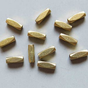 Puede incluir: Una colección de 12 tapones de extremo de metal de color dorado para la elaboración de joyas. Los tapones de extremo son de forma ovalada y tienen una superficie texturizada.
