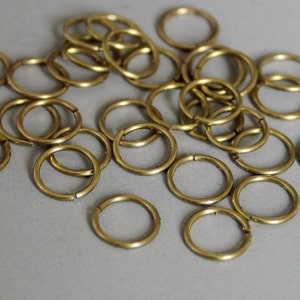 May include: A large pile of gold-colored metal jump rings. The rings are of various sizes and are scattered on a white surface.