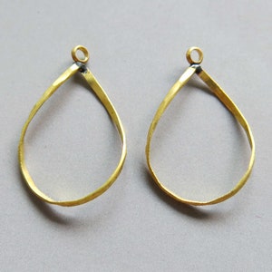 Puede incluir: Dos aros de pendientes de metal dorado en forma de lágrima. Los aros son lisos y tienen una textura ligeramente martillada.