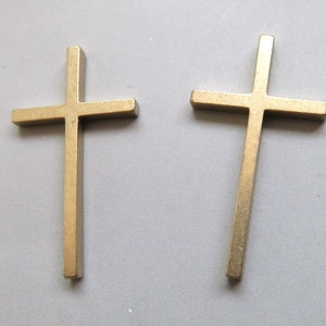 Puede incluir: Dos cruces de metal de color dorado. Las cruces son de diseño simple y tienen un acabado liso y pulido.