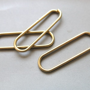 May include: Three gold-colored metal rings, each with a rounded oval shape. The rings are stacked on top of each other.