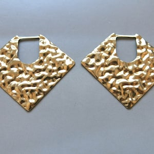 May include: A pair of gold-toned square hoop earrings with a hammered texture. The earrings have a large, open, square shape.