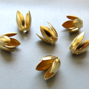 Pode incluir: Seis enfeites de metal dourado em forma de flor. Cada enfeite tem duas pétalas abertas e duas pétalas fechadas.