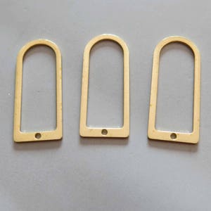 Könnte beinhalten: Drei goldfarbene Metallanhänger mit abgerundeten Oberseiten und einem Loch in der Mitte. Die Anhänger sind rechteckig und haben eine glatte, polierte Oberfläche.