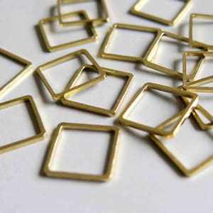 Puede incluir: Una colección de anillas de salto cuadradas de metal dorado. Las anillas son de varios tamaños y están esparcidas sobre una superficie blanca.