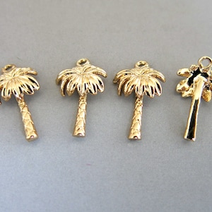 Op de afbeelding: Vier goudkleurige palmboombedels. Elke bedel heeft gedetailleerde palmbladeren en een getextureerde stam, met een kleine lus aan de bovenkant om aan sieraden of andere knutselwerken te bevestigen. De bedels worden tegen een grijze achtergrond weergegeven.