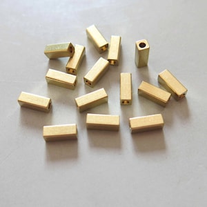 May include: A group of 14 gold-coloured metal spacers, each with a rectangular shape and two holes. The spacers are arranged in a random pattern on a white surface.