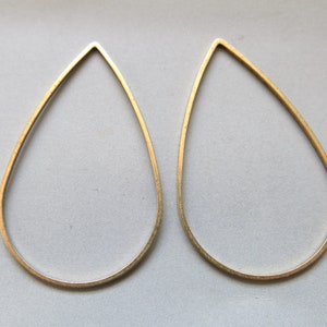May include: Two gold-colored, teardrop-shaped earrings. The earrings are made of thin metal and have a simple, minimalist design. The teardrop shape is elongated and symmetrical, with a pointed top and rounded bottom. The earrings are displayed against a neutral background.