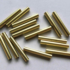 May include: A group of 15 gold-colored metal tubes, approximately 1 inch in length, are scattered on a white surface.