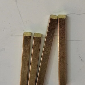May include: Four gold-colored metal rods with square cross-sections. The rods are arranged vertically, with the top ends aligned.