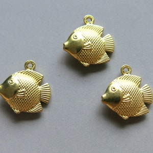 Puede incluir: Tres abalorios de pescado de metal dorado con superficie texturizada. Los peces tienen un cuerpo redondeado y una pequeña aleta caudal.