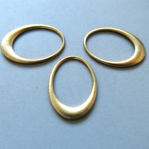 Peut inclure: Trois anneaux en métal de couleur dorée, chacun avec une forme légèrement différente. Les anneaux sont disposés en forme de triangle sur une surface bleu clair.
