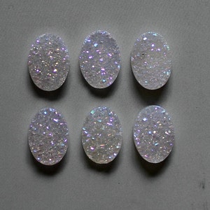 Può includere: Sei cabochon ovali bianchi con glitter iridescente. I cabochon misurano circa 2,5 cm di lunghezza.