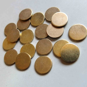 Op de afbeelding: Een verzameling kleine, ronde, metaal goudkleurige schijfjes verspreid op een lichtgrijze ondergrond. De schijfjes lijken van metaal te zijn en hebben een glad, plat oppervlak. Het algemene effect is een stapel glanzende, gouden munten of decoratieve elementen.