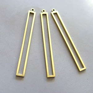 May include: Three gold-colored metal bar pendants with a rectangular opening. The pendants have a loop at the top for attaching to a chain or cord.