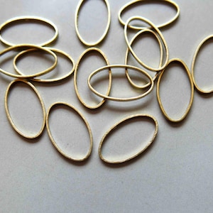 May include: A group of oval-shaped metal rings, all gold in color, are scattered on a light gray surface. The rings are of varying sizes and are arranged in a random pattern.