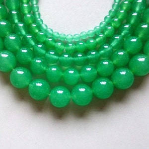 May include: A strand of green jade beads in various sizes, arranged in a circular pattern. The beads are smooth and polished, with a subtle sheen.